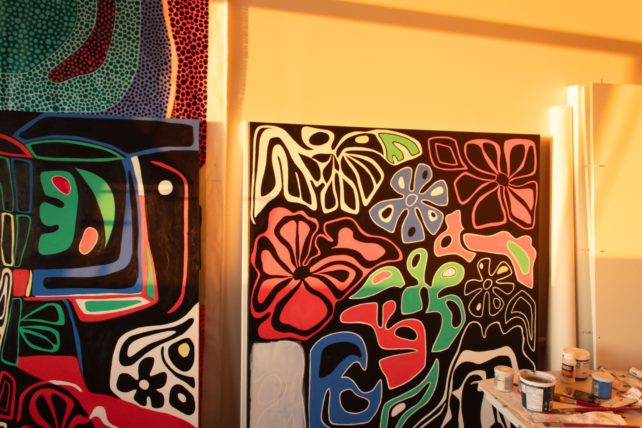 Sunlit paintings beside a table of paints and brushes